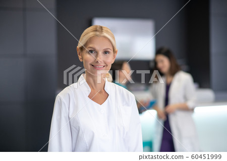 Mature blonde doctor in white robe smiling Mature blonde doctor in white robe smiling 60451999