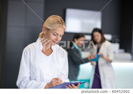 Mature blonde doctor in white robe looking busy 60452002