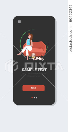 woman sitting on armchair happy girl with dog relaxing at home smartphone screen online mobile app full length vertical 60452345