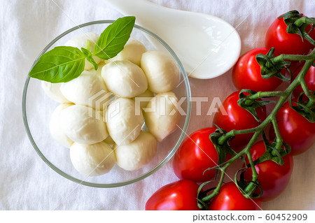 Mini mozzarella cheese balls in glass bowl and branch of red cherry tomatoes. 60452909
