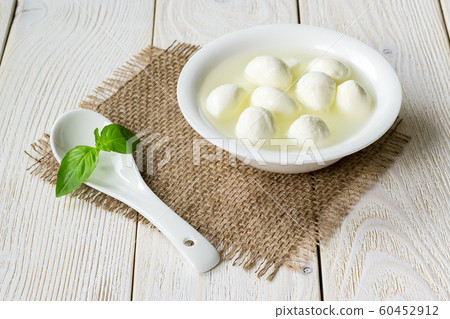 White bowl with small mozzarella cheese balls in a brine and porcelain spoon. White bowl with small mozzarella cheese balls in a brine and porcelain spoon. 60452912