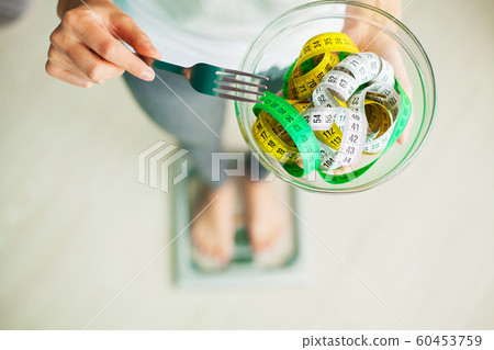 Diet and Weight Loss. Woman holds bowl and fork with measuring tape Diet and Weight Loss. Woman holds bowl and fork with measuring tape 60453759
