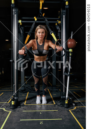 Front view of confident young blonde woman doing weight lifting workout Attractive young woman lifting weight looking forward Strong trained body shape arms chest legs. 60454018