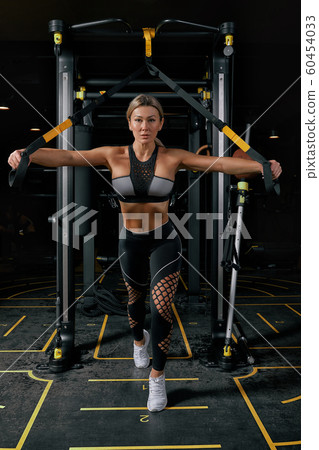 Front view of confident young blonde woman doing weight lifting workout Attractive young woman lifting weight looking forward Strong trained body shape arms chest legs. 60454033
