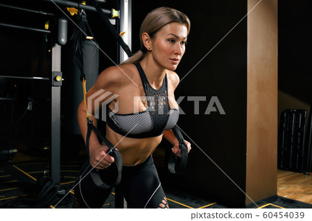 Front view of confident young blonde woman doing weight lifting workout Attractive young woman lifting weight looking forward Strong trained body shape arms chest legs. Front view of confident young blonde woman doing weight lifting workout Attractive young woman lifting weight looking forward Strong trained body shape arms chest legs. 60454039