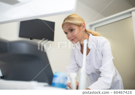 Blond pretty ultrasound specialist in white robe looking busy 60467428