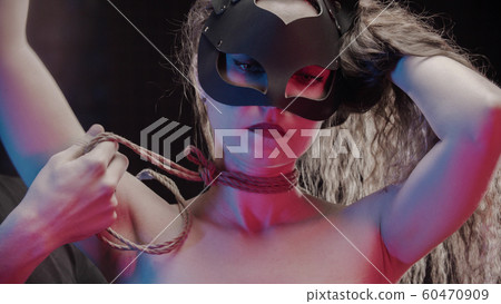 shibari - a man making knots on woman's neck in neon lighting shibari - a man making knots on woman's neck in neon lighting 60470909