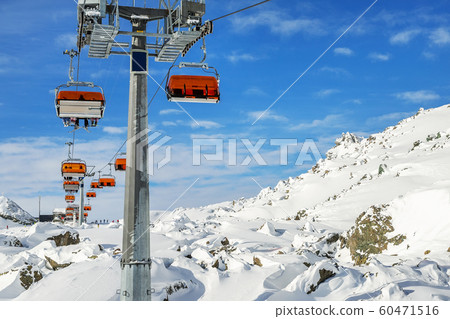 Ski lift ropeway on hilghland alpine mountain winter resort on bright sunny day. Ski chairlift cable way with people enjoy skiing and snowboarding. downhill slopes and virgin snow off-piste area Ski lift ropeway on hilghland alpine mountain winter resort on bright sunny day. Ski chairlift cable way with people enjoy skiing and snowboarding. downhill slopes and virgin snow off-piste area 60471516