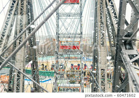 aerial red cabin view and steel frame construction of oldest ferris wheel in Vienna Prater amusement fair park during cold snowy winter day. Snowfall blizzard weather in european city 60471602