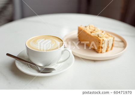 Slice of caramel cake and a fork on the right side. A cup of hot coffee with ground in the background.Close-up 60471970