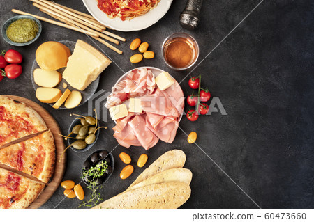 Italian food with copy space. Pizza, pasta, cheese, ham, wine, olives, pesto, capers, shot from above with a place for text, a flat lay on a dark background Italian food with copy space. Pizza, pasta, cheese, ham, wine, olives, pesto, capers, shot from above with a place for text, a flat lay on a dark background 60473660