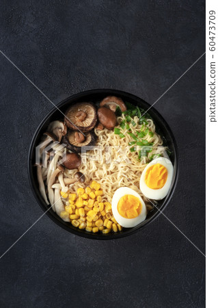 Ramen noodle soup. Soba noodles with eggs, shiitake and enoki mushrooms, corn and scallions, overhead shot on a black background with copy space 60473709
