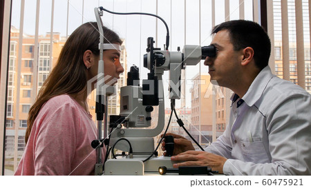 Ophthalmology treatment - young woman checking her visual acuity with a special equipment in the bright cabinet Ophthalmology treatment - young woman checking her visual acuity with a special equipment in the bright cabinet 60475921