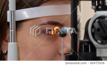 Ophthalmology treatment - a young woman checking her visual acuity with a light of special big optometry machine - brown eyes color 60475938