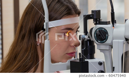 Ophthalmology treatment - a young woman checking her visual acuity with a light of special big optometry machine Ophthalmology treatment - a young woman checking her visual acuity with a light of special big optometry machine 60475940
