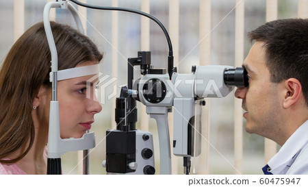 Ophthalmology treatment - young woman checking her visual acuity with a special equipment in the bright cabinet Ophthalmology treatment - young woman checking her visual acuity with a special equipment in the bright cabinet 60475947