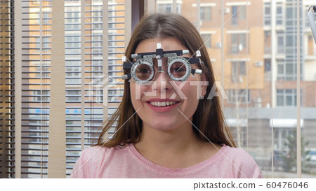 Ophthalmology treatment - a young smiling woman sitting in the optometry device for vision test Ophthalmology treatment - a young smiling woman sitting in the optometry device for vision test 60476046