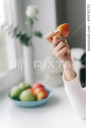Woman hand holds an apple in front of a window, close-up 60476152