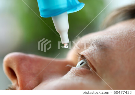 Man putting liquid drops in his eye solving vision problem Man putting liquid drops in his eye solving vision problem 60477433