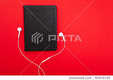 Black notebook with white earphones isolated on red background Black notebook with white earphones isolated on red background 60478146