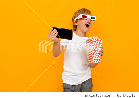 admiring boy in glasses for a movie theater with popcorn and a telephone on a yellow background admiring boy in glasses for a movie theater with popcorn and a telephone on a yellow background 60479113