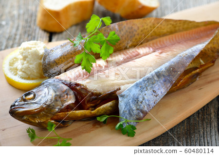 A smoked rainbow trout served on a wooden cutting board with horseradish, parsley,lemon and baguette 60480114