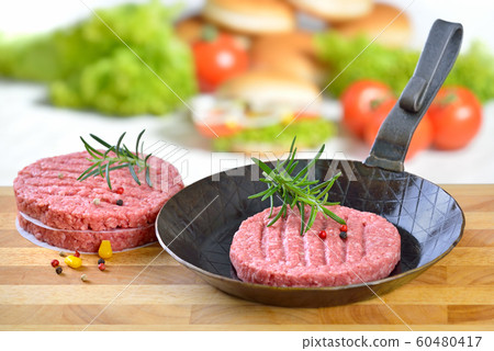 Raw burger patty in an iron frying pan ready to fry, some burger ingredients in the background Raw burger patty in an iron frying pan ready to fry, some burger ingredients in the background 60480417