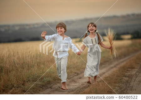 Brother and sister village children running barefoot on a rural road 60480522