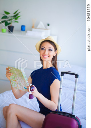 Vacation. Woman Who is Preparing for Rest. Young Beautiful Girl Sits on the Bed and Holds in the Hands Map. Portrait of a Smiling Woman. Happy Girl Goes On Vacation 60481859
