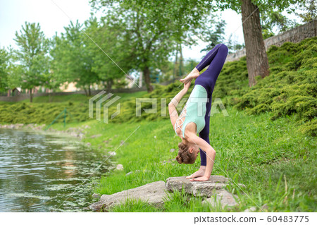 A young sports girl practices yoga on a green lawn A young sports girl practices yoga on a green lawn 60483775