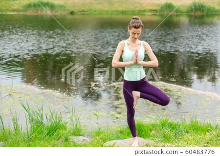 A young sports girl practices yoga on a green lawn 60483776