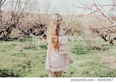 blonde in pink dress walks in the garden with flowering trees 60483967