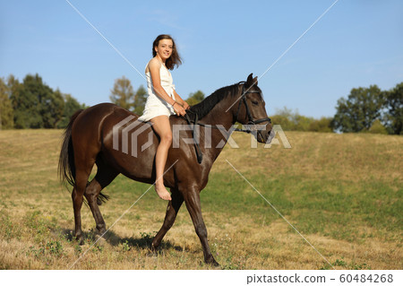 Happy young girl in white dress galloping on horse 60484268