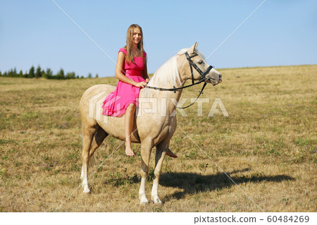 Portrait of young girl in pink dress sit on ponny 60484269