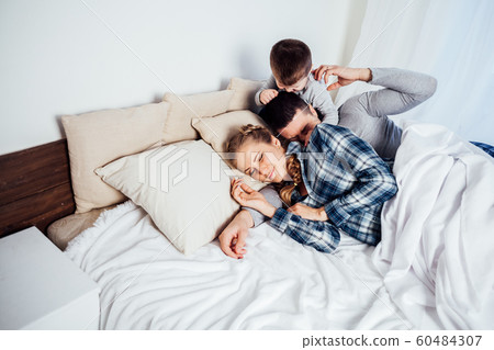 mom dad and son in the morning lying on the bed at home in a good mood 60484307