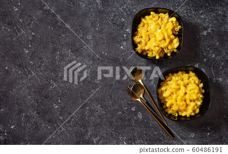 Mac and cheese into two black bowls on dark 60486191
