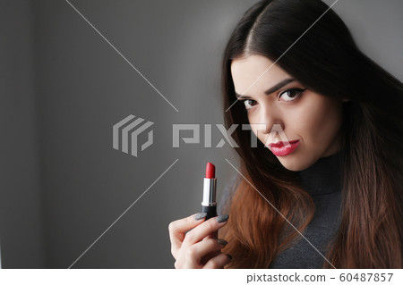 Beautiful young woman putting lipstick on lips Beautiful young woman putting lipstick on lips 60487857