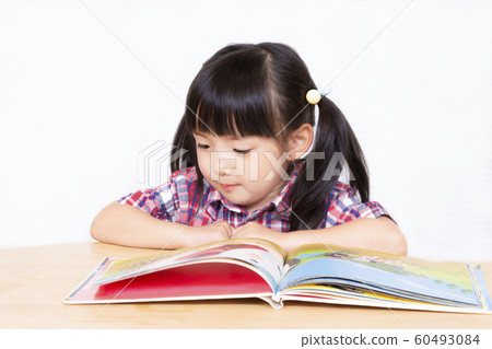Little girl reading a book in front of a white background. Infant, education, reading, learning, growth, childcare image 60493084