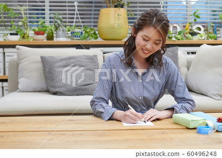 Young woman wrapping a gift by writing a message card 60496248