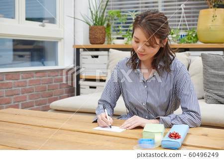 Young woman wrapping a gift by writing a message card 60496249