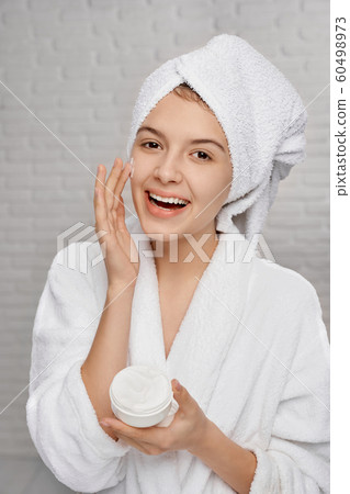 Portrait of happy female in towel applying cream face Portrait of happy female in towel applying cream face 60498973