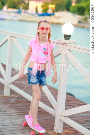 A cheerful girl with a skateboard walks and has fun in the outdoor area 60501067