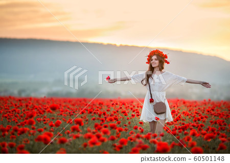 A woman in an agricultural field with a wreath on her head of red poppies 60501148