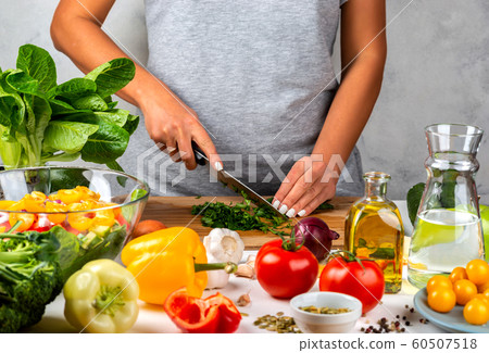 Woman cuts greens and cooking salad in the kitchen. Healthy diet concept. 60507518