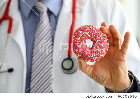 Doctor in office holding in hand pink doughnut Doctor in office holding in hand pink doughnut 60508680