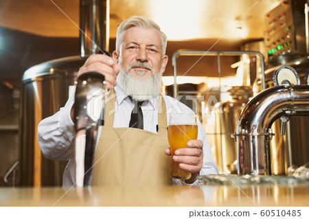 Elderly barman standing at bar counter with beer glass. Elderly barman standing at bar counter with beer glass. 60510485