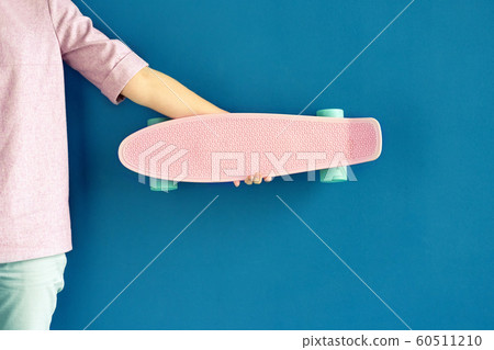 Woman holding pink plastic skateboard against deep blue wall 60511210