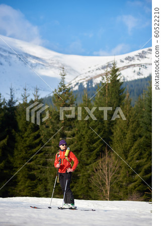 Male skier on skis on background of spruce trees and snowy mountain peak on frosty sunny winter day. Male skier on skis on background of spruce trees and snowy mountain peak on frosty sunny winter day. 60522210