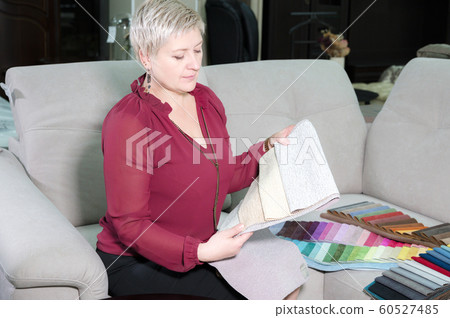 Stylish stylish woman with a short haircut sits on a sofa in a furniture store and looks at upholstery probes. She chooses furniture for herself 60527485