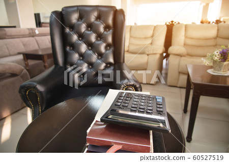 The workplace of the director of a furniture store with an expensive leather armchair, a sofa table and several catalogs of furniture and a calculator. The concept of a cozy workplace The workplace of the director of a furniture store with an expensive leather armchair, a sofa table and several catalogs of furniture and a calculator. The concept of a cozy workplace 60527519